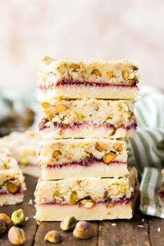 a stack of four pieces of cake sitting on top of a wooden table next to pistachios