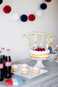 a birthday cake and cupcakes on a table with balloons in the shape of letters