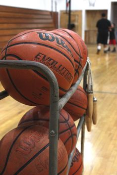 several basketballs are stacked on top of each other in a gym with people walking by