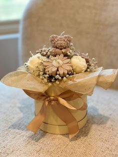 a bouquet of flowers in a gold box on a table with a brown ribbon around it