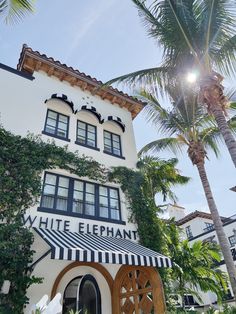 a white building with black and white striped awning next to palm trees in front of it