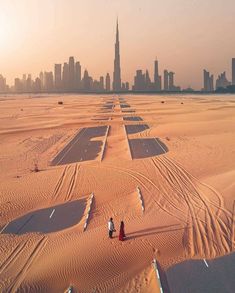 two people standing in the middle of an empty desert with skyscrapers in the background