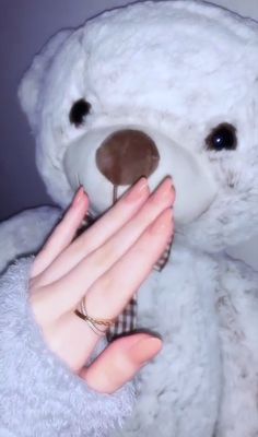 a white teddy bear is being held by a woman's hand with her right hand