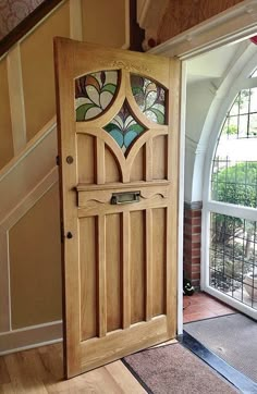 an open wooden door sitting inside of a room next to a stair case with stained glass panels