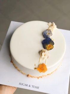 a white cake with blue and orange flowers on it's side is being held up by a hand