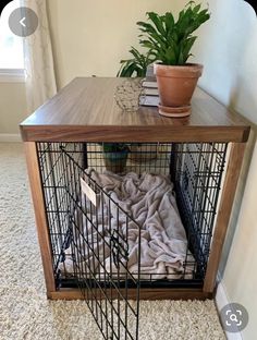 a dog crate with a blanket on top and a potted plant next to it