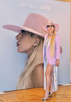 a woman in a pink hat and silver skirt standing next to a wall with a poster on it