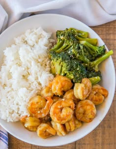 a white bowl filled with shrimp and broccoli next to rice on top of a wooden table