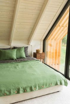 a bed with green sheets and pillows in a bedroom next to an open glass window