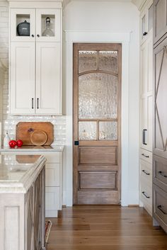 a wooden door in a white kitchen with wood flooring and cabinet doors on both sides