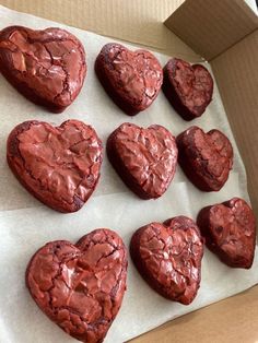 twelve heart shaped cookies in a box on top of a piece of parchment paper with chocolate frosting