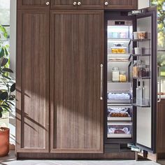 an open refrigerator in a kitchen with lots of cupboard space and plants on the counter