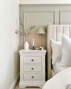 a white nightstand with two candles on it next to a bed