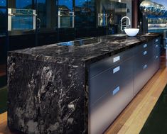 a large black marble counter top in a room with wooden floors and glass doors on the walls