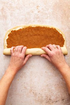 two hands are rolling out the dough on top of an uncooked pizza crust