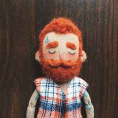 a red haired doll with a beard and plaid shirt is posed on a wooden surface