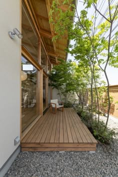 a wooden deck in front of a white building with trees and rocks on the ground