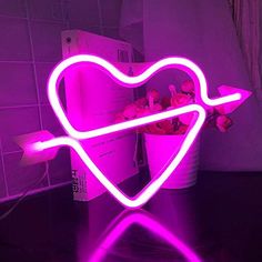 a heart shaped neon sign sitting on top of a table next to a flower pot