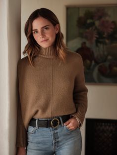 a woman standing next to a wall wearing a brown sweater and jeans