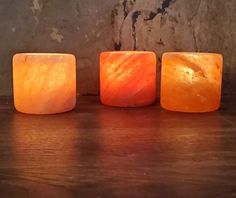 three square candles sitting on top of a wooden table next to a stone wall and floor