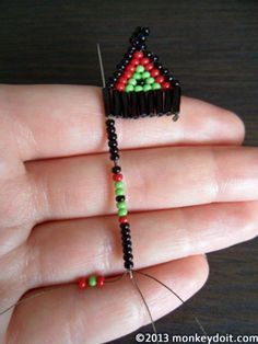 a hand holding a beaded string with a triangle shaped pincust attached to it