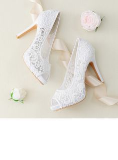 two pairs of white high heel shoes next to a rose and ribbon on a table