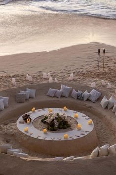 an outdoor seating area on the beach with candles and flowers arranged in the sand around it