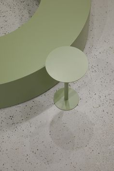 a green curved bench sitting on top of a cement floor next to a white wall