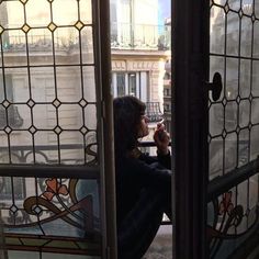 a woman sitting on the window sill drinking from a cup in front of her