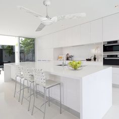 a modern kitchen with white cabinets and counter tops, along with bar stools in front of the island