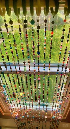 a window with beads hanging from it's side in front of a lush green field