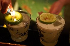 someone lighting a candle on top of two glasses filled with liquid and limes in them