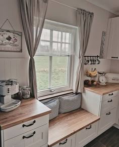 a kitchen with white cabinets and wooden counter tops next to a large window in the corner