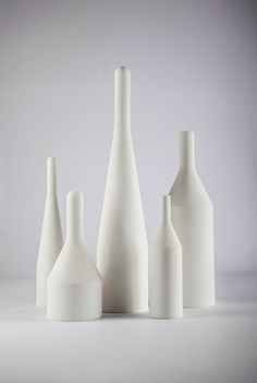 five white vases are lined up against a gray background, with one empty bottle in the foreground