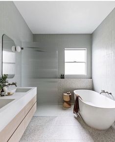 a white bath tub sitting under a bathroom window next to a sink and a mirror