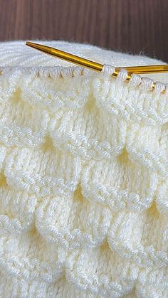 there is a crochet stitch on the edge of a white blanket next to a knitting needle