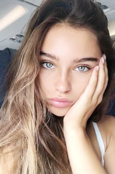 a woman with long hair and blue eyes is sitting in an airplane looking at the camera