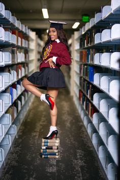 a woman in a graduation cap and skirt jumping on stacks of books with her legs spread out