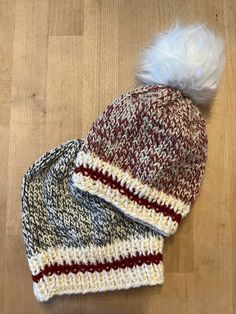 two knitted hats sitting on top of a wooden floor with a white and red pom - pom