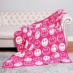 a white couch sitting next to a pink blanket on top of a rug covered in smiley faces