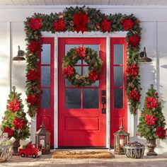 a red front door decorated for christmas with poinsettis and wreaths on it