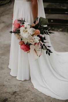 a woman in a white dress holding a bridal bouquet with flowers and greenery