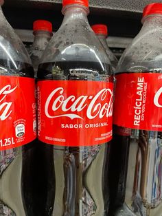 three bottles of coca - cola are on display in a grocery store, one is red and the other is black