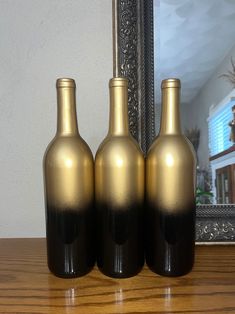 three black and gold bottles sitting on top of a wooden table next to a mirror