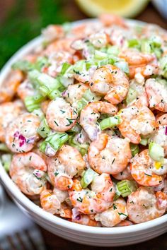 a white bowl filled with shrimp and celery on top of a wooden table