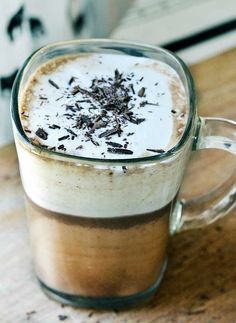 a glass mug filled with liquid and chocolate shavings on top of a wooden table