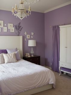 a bedroom with purple walls, white bedding and a chandelier hanging from the ceiling