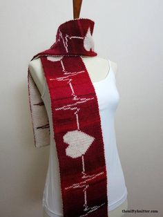 a red and white knitted scarf hanging on a mannequin