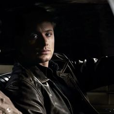 a man in a leather jacket sitting in a car