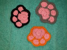 three crocheted animal paw prints are shown on a green surface, one is pink and the other is black